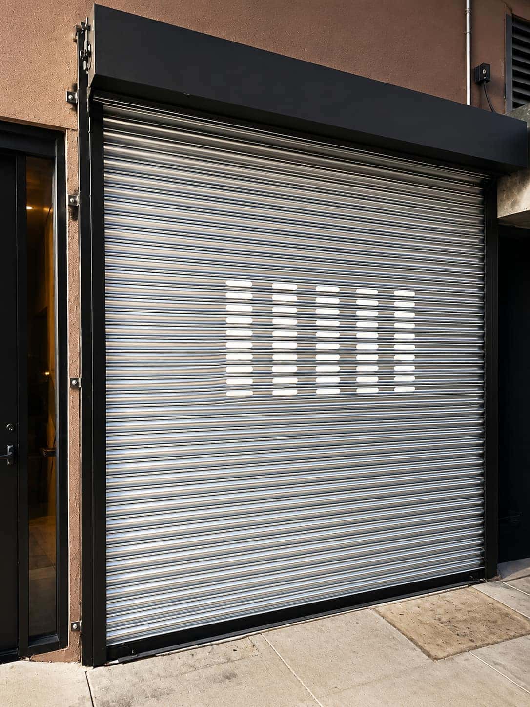 Perforated rolling steel security gate closed across a commercial storefront in daylight